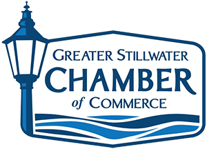 Logo of the Greater Stillwater Chamber of Commerce featuring a blue streetlamp on the left and stylized waves under the organizations name in bold blue text.